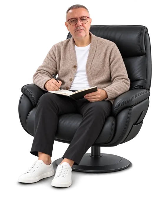 João André com cardigan taupe, caderno e caneta no colo, sentado na poltrona preta.