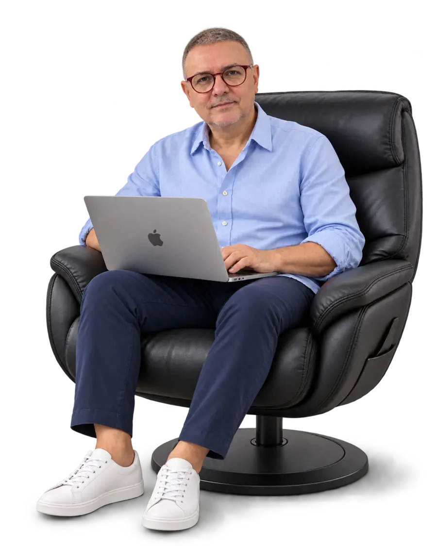 João André com camisa Oxford azul e notebook aberto no colo, sentado na poltrona preta.