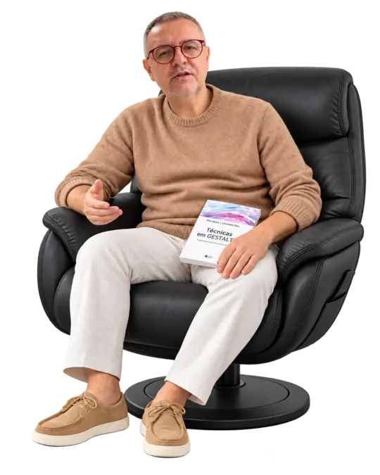 João André com malha camel e livro no colo, fazendo um pequeno gesto de conversa.